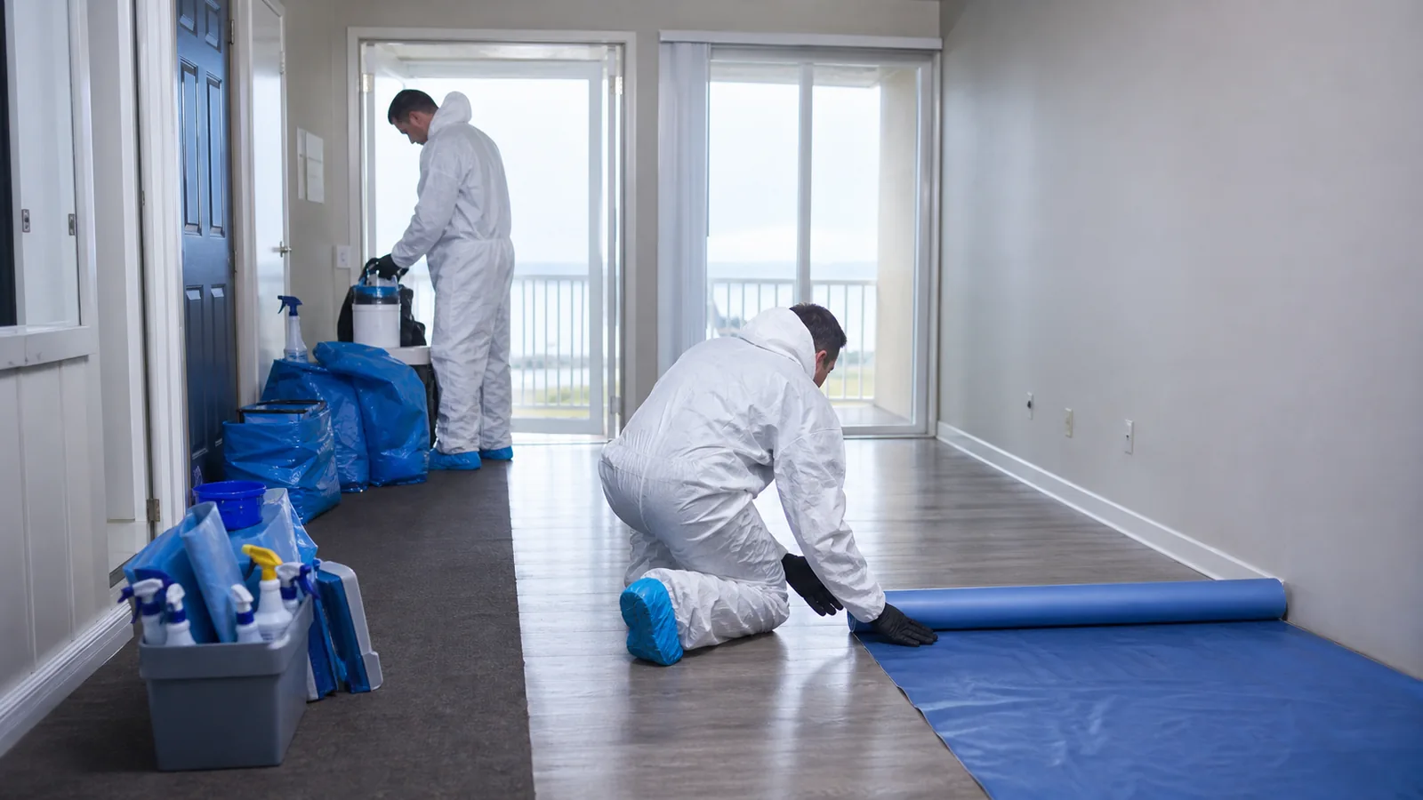 Illustrative remediation team organizing protective supplies in a released apartment